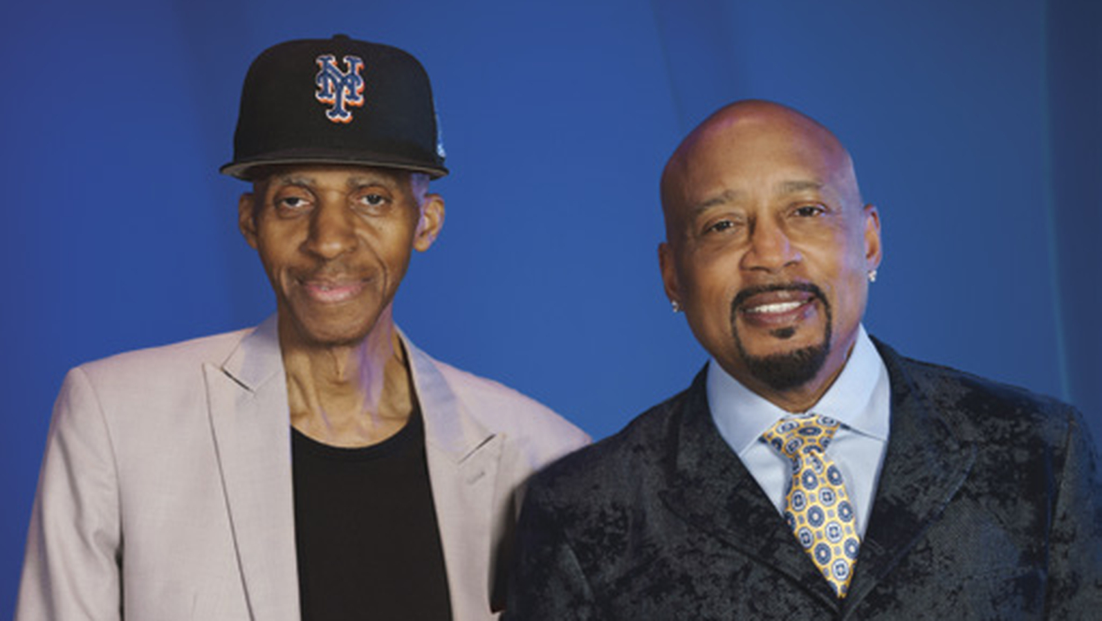 Daymond John and his mentor Charles Fisher posing together in front of a blue backdrop