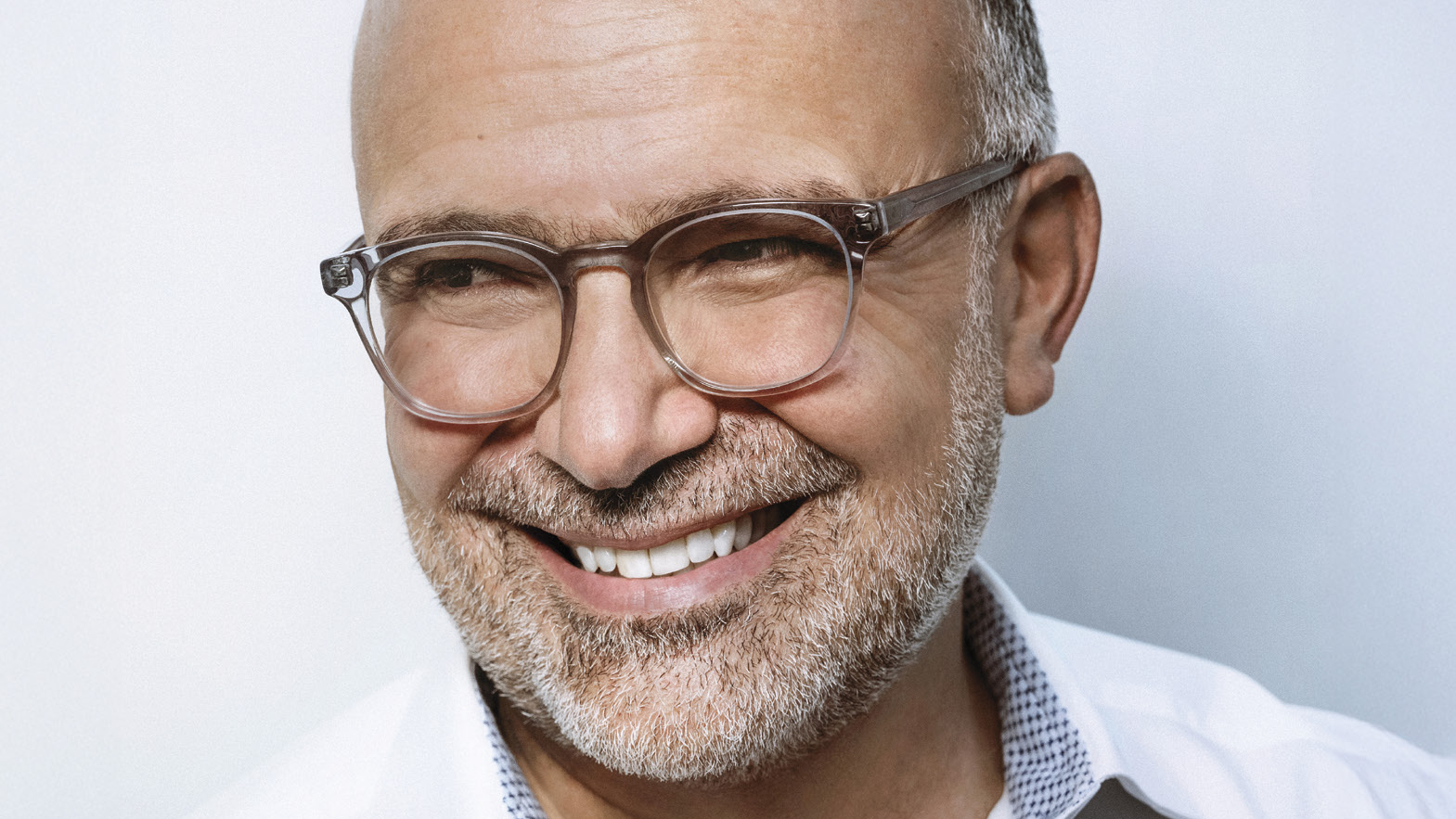 Manuel Abud smiling in glasses and a white open-collar shirt